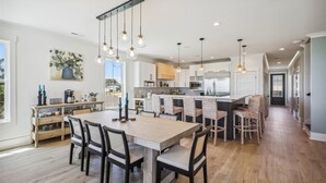 A modern kitchen with a central island, pendant lighting, and a dining area with a wooden table and chairs. - Atlantic Oasis - Oceanview - Pool & Hot Tub - 6 Bed (North Myrtle Beach)