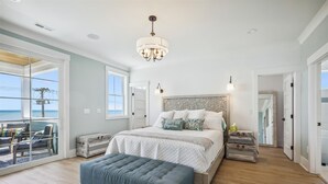 A spacious bedroom with a large bed, a chandelier, and a view of the ocean through a sliding glass door. - Atlantic Oasis - Oceanview - Pool & Hot Tub - 6 Bed (North Myrtle Beach)