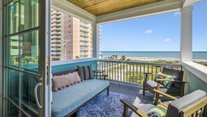 A balcony with a wooden ceiling, a sofa, two chairs, and a view of the ocean and buildings. - Atlantic Oasis - Oceanview - Pool & Hot Tub - 6 Bed (North Myrtle Beach)