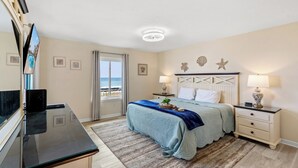 Ein Schlafzimmer mit Bett, Nachttischen, einem Fernseher und Blick auf den Strand.