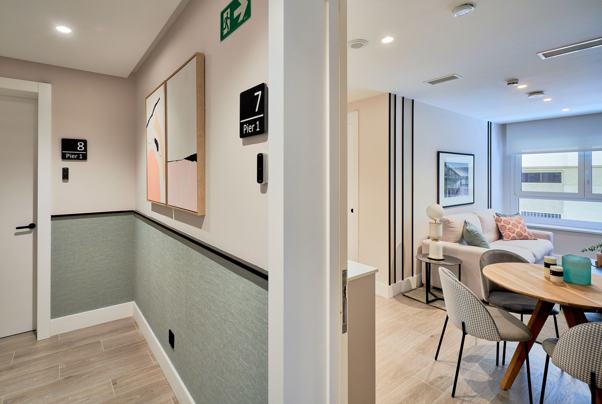Un couloir d’hôtel avec un mur recouvert de carreaux verts, un plancher en bois et un coin repas comprenant une table ronde et des chaises.