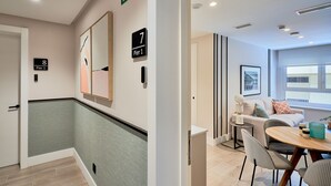 A hotel corridor with a green-tiled wall, a wooden floor, and a dining area with a round table and chairs. - iloftmalaga Muelle Uno VII (Málaga)
