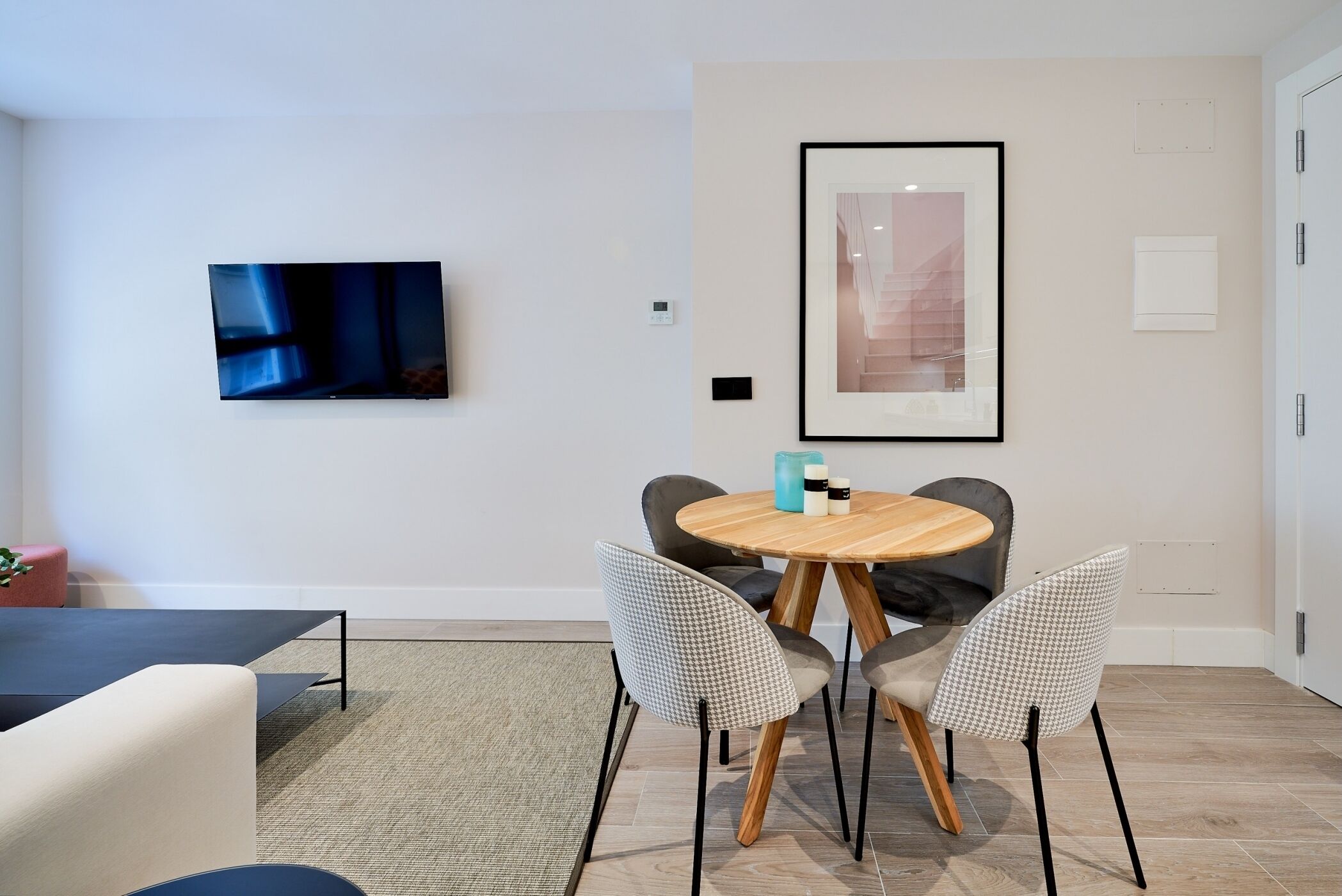 Un comedor moderno con una mesa de madera redonda, dos sillas estampadas, un televisor de pantalla plana y un cuadro en la pared.