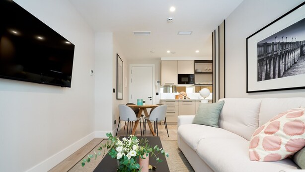 A modern living room with a flat-screen TV, a sofa with patterned cushions, a coffee table with a floral arrangement, and a dining area with a table and chairs. - iloftmalaga Muelle Uno VII (Málaga)