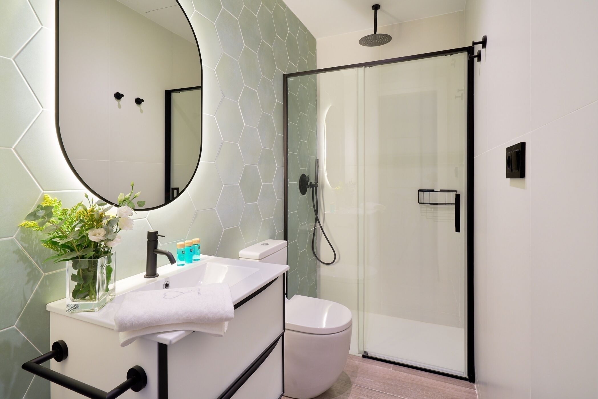 Een moderne badkamer met een douchecabine van glas, een wit wastafelmeubel met spiegel en een toilet.