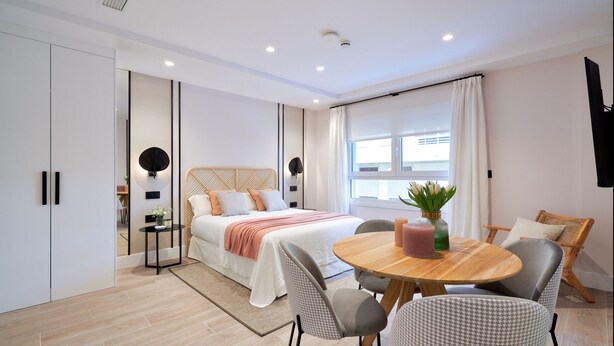 A modern bedroom with a bed, bedside tables, a round wooden table with chairs, and a large window with curtains. - iloftmalaga Muelle Uno VI (Málaga)