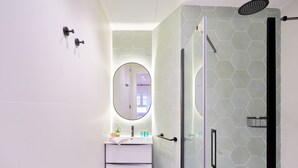 A modern bathroom with a glass-enclosed shower, a white vanity with a round mirror, and hexagonal patterned walls. - iloftmalaga Muelle Uno VI (Málaga)