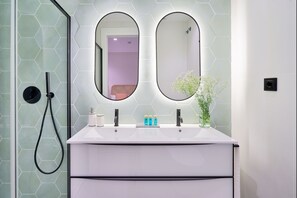 A bathroom with a white vanity, two oval mirrors, a handheld showerhead, and a vase with flowers. - iloftmalaga Muelle Uno V (Málaga)