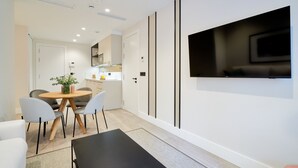 Una sala de estar moderna con una mesa de centro negra, una mesa de comedor redonda con sillas a cuadros, y un televisor de pantalla plana montado en la pared.