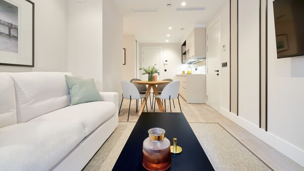 Una sala de estar moderna con un sofá blanco, una mesa de comedor con sillas y una cocina al fondo.