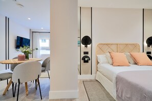 A modern hotel room with a wooden headboard, a bed with two pillows, a bedside table with a pink candle, and a wall-mounted light fixture. - iloftmalaga Muelle Uno V (Málaga)