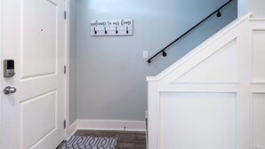 A hallway with a light blue wall, a welcome sign, a black metal handrail, and a patterned rug.