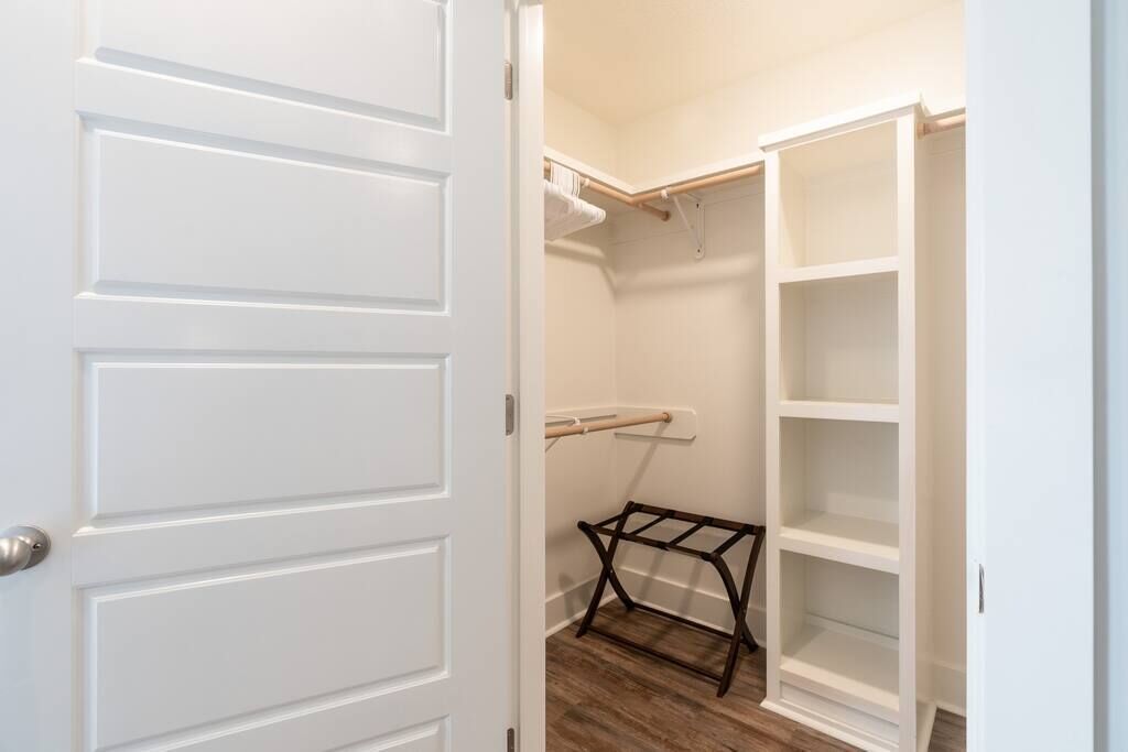 A walk-in closet with white shelving units and a wooden rack.
