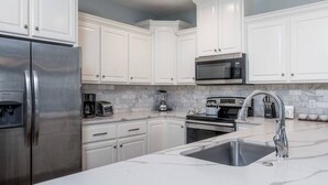 A modern kitchen with white cabinets, stainless steel appliances, and a marble countertop.