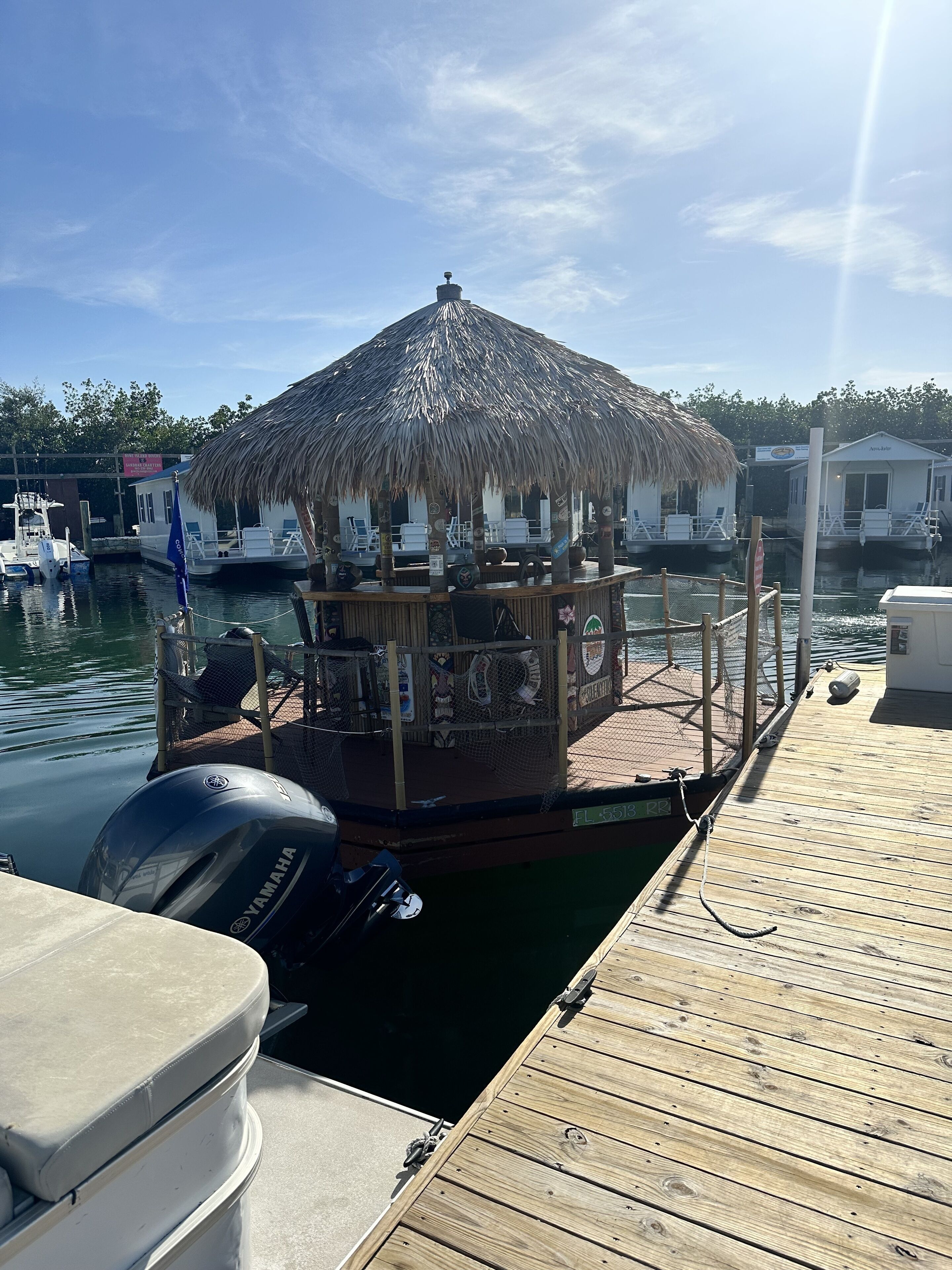 A docked boat with a thatched-roof structure, a Yamaha outboard motor, and a wooden deck.