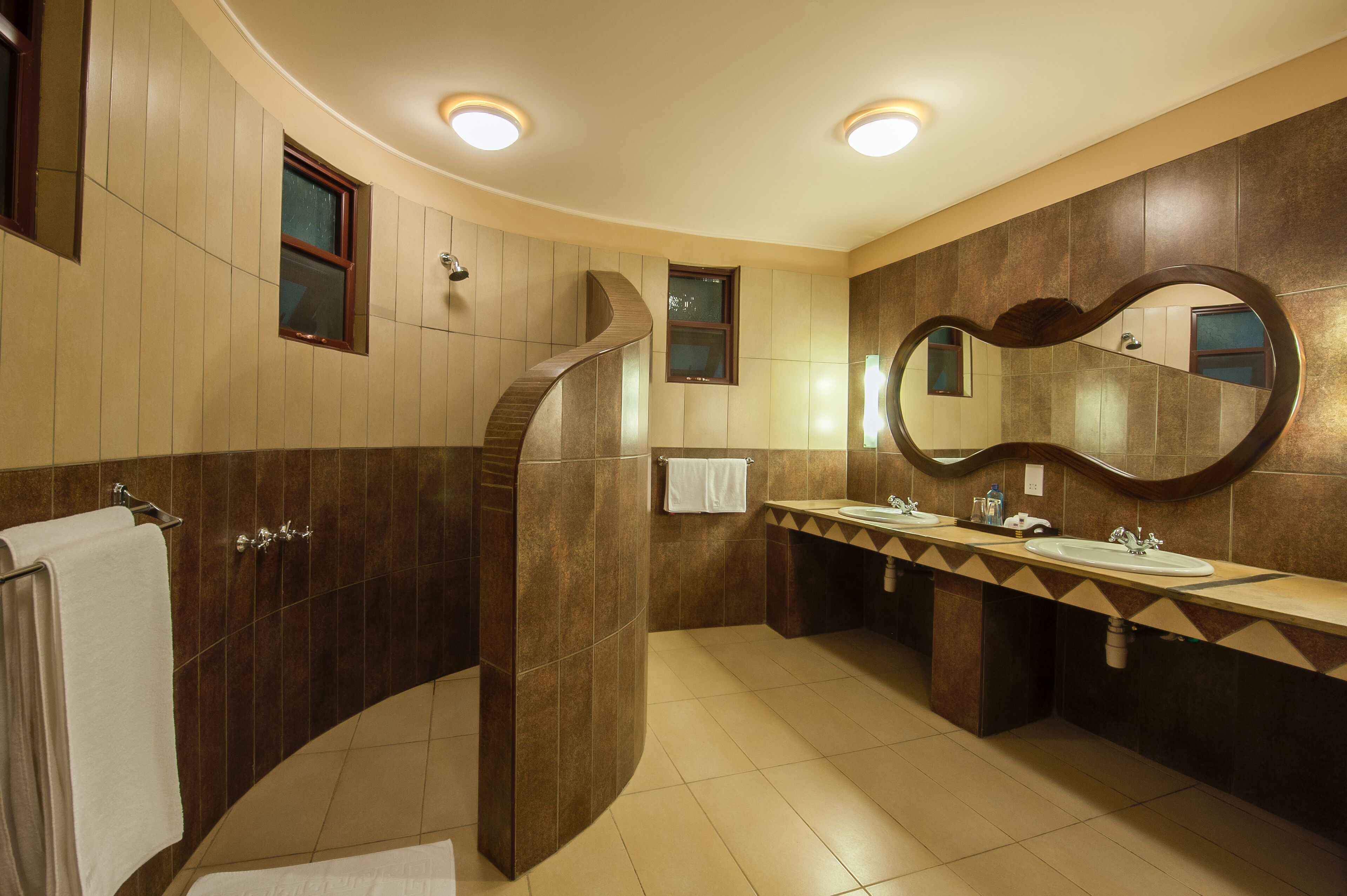 Een moderne badkamer met een gebogen douche, twee wastafels en een grote spiegel.