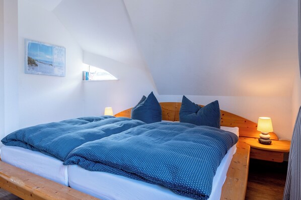 A bedroom with a wooden bed, a nightstand with a lamp, and a wall-mounted picture.