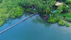 Vue aérienne d’un complexe hôtelier tropical, avec une longue jetée en bois s’étendant dans un lagon aux eaux bleu cristallin, le tout entouré d’une végétation luxuriante et de palmiers.