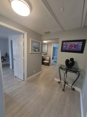 A hallway with a door leading to a room, a chair, a table with a sculpture, and two framed pictures on the wall.