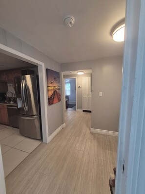 A modern kitchen with stainless steel appliances, a hallway with wooden flooring, and a door leading to another room.