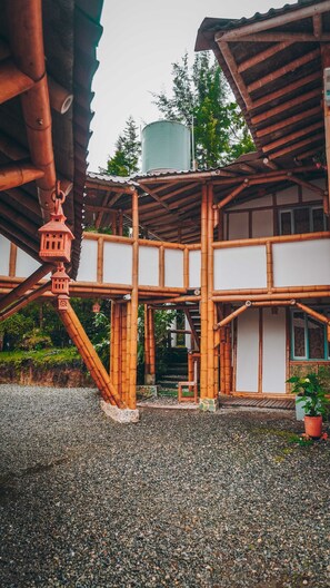A traditional wooden structure with a bamboo framework, a water tank, and a gravel ground.