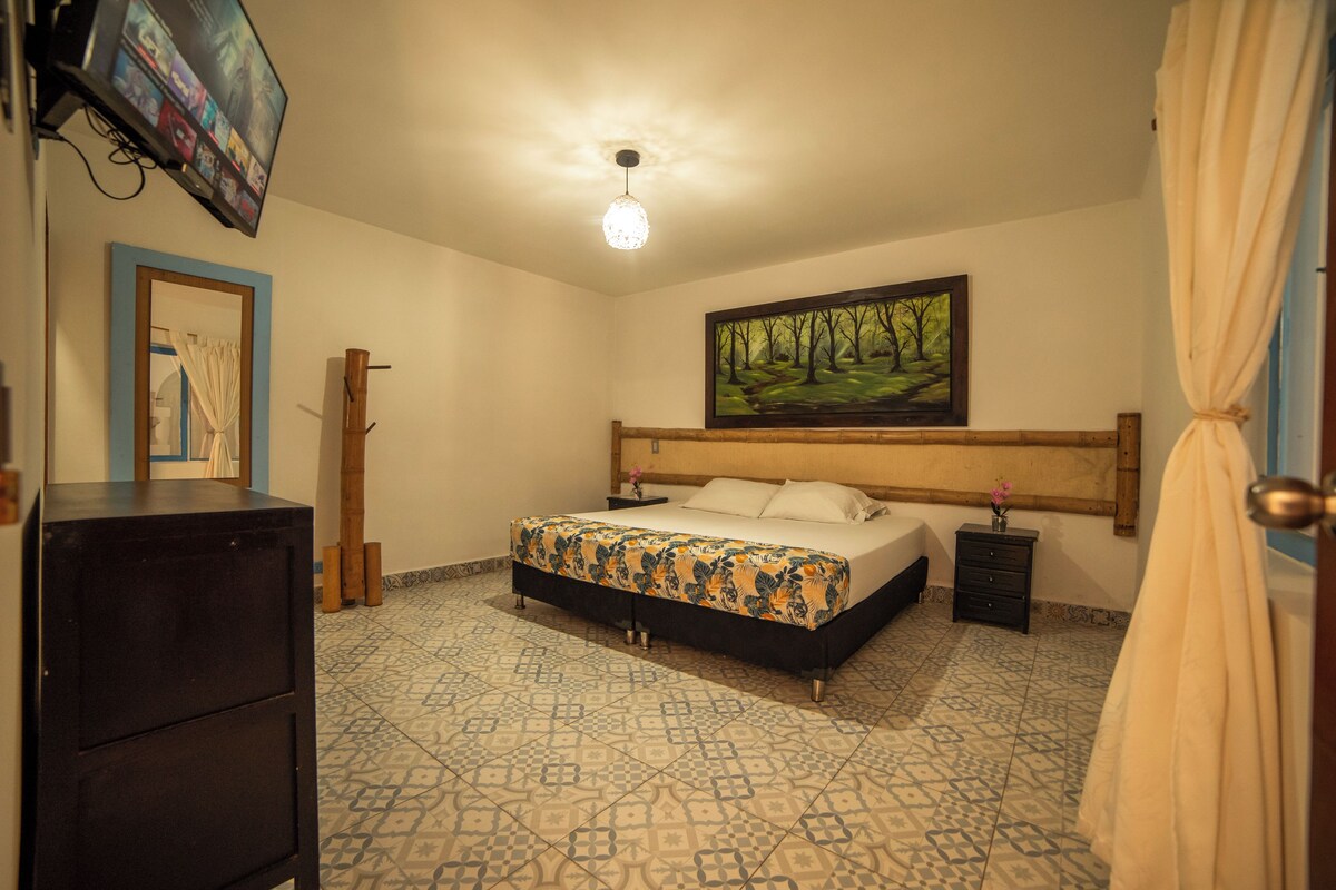 A bedroom with a bed, a television mounted on the wall, a painting above the bed, and a patterned floor.