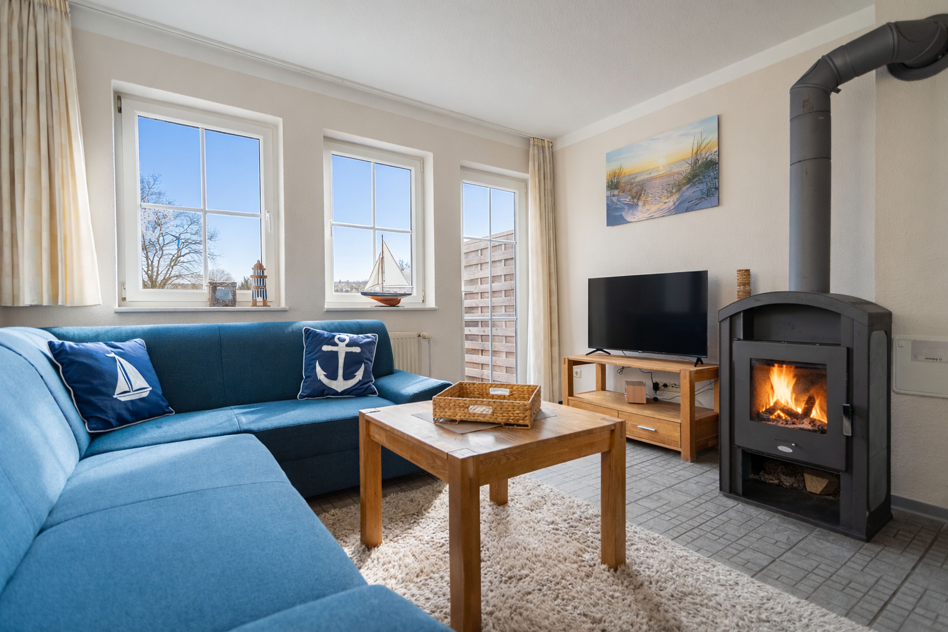 A living room with a blue sofa, a television, a fireplace, and large windows.