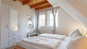 A bedroom with two beds, a wooden bench, a wardrobe, and a window with curtains. - House Boddenkieker 2 Rügen Mönchgut, terrace with great lake view, Göhren. Sellin (Mönchgut)
