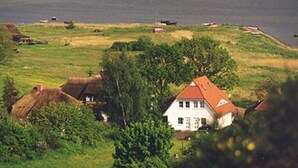 A rural landscape with a house near a body of water, surrounded by fields and trees. - House Boddenkieker 2 Rügen Mönchgut, terrace with great lake view, Göhren. Sellin (Mönchgut)