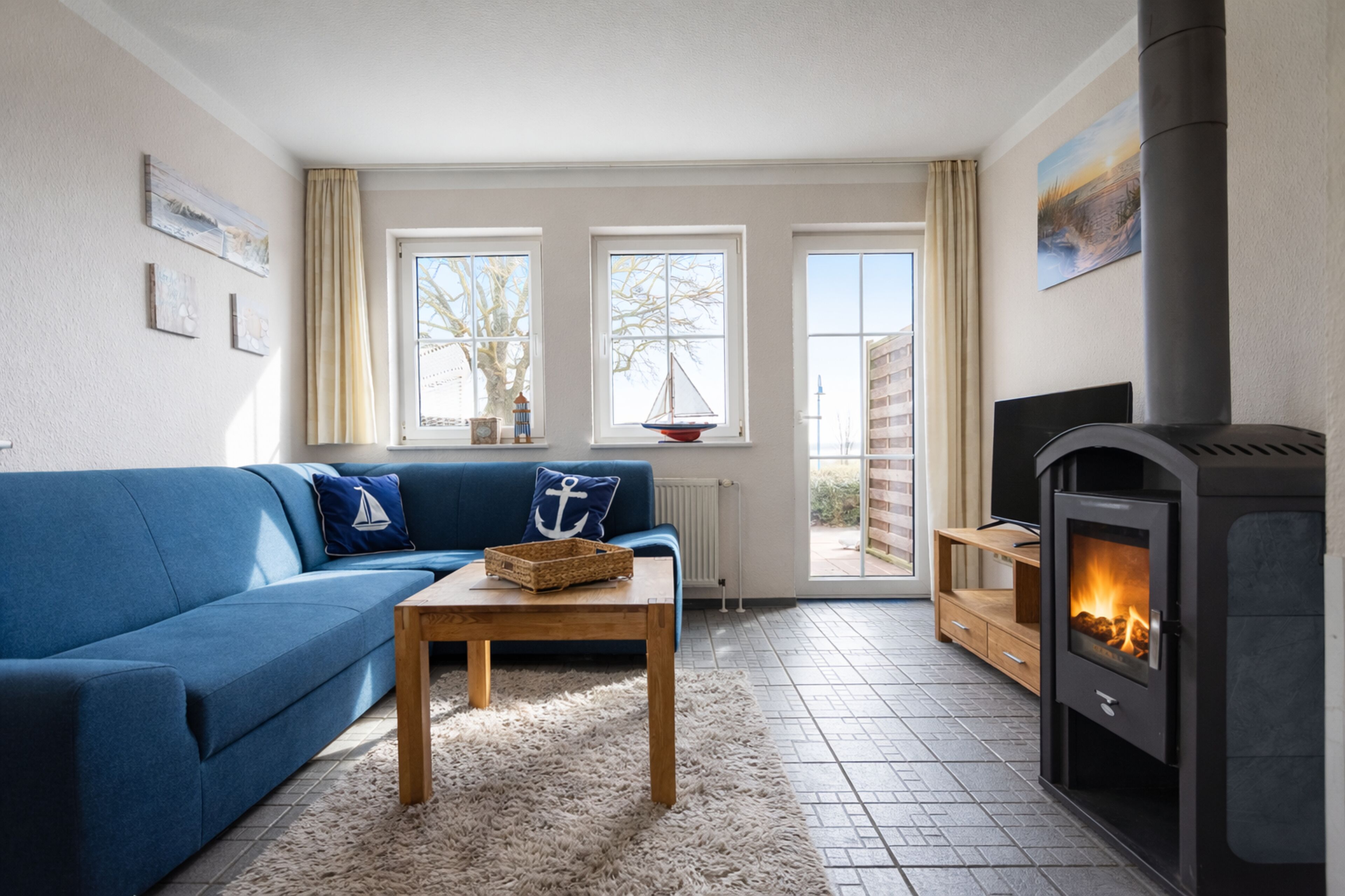 Ein Wohnzimmer mit blauem Sofa, einem Holztisch, einem Kamin und großen Fenstern.