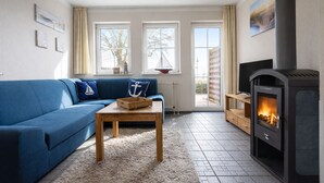 A living room with a blue sofa, a wooden coffee table, a fireplace, and large windows. - House Boddenkieker 2 Rügen Mönchgut, terrace with great lake view, Göhren. Sellin (Mönchgut)
