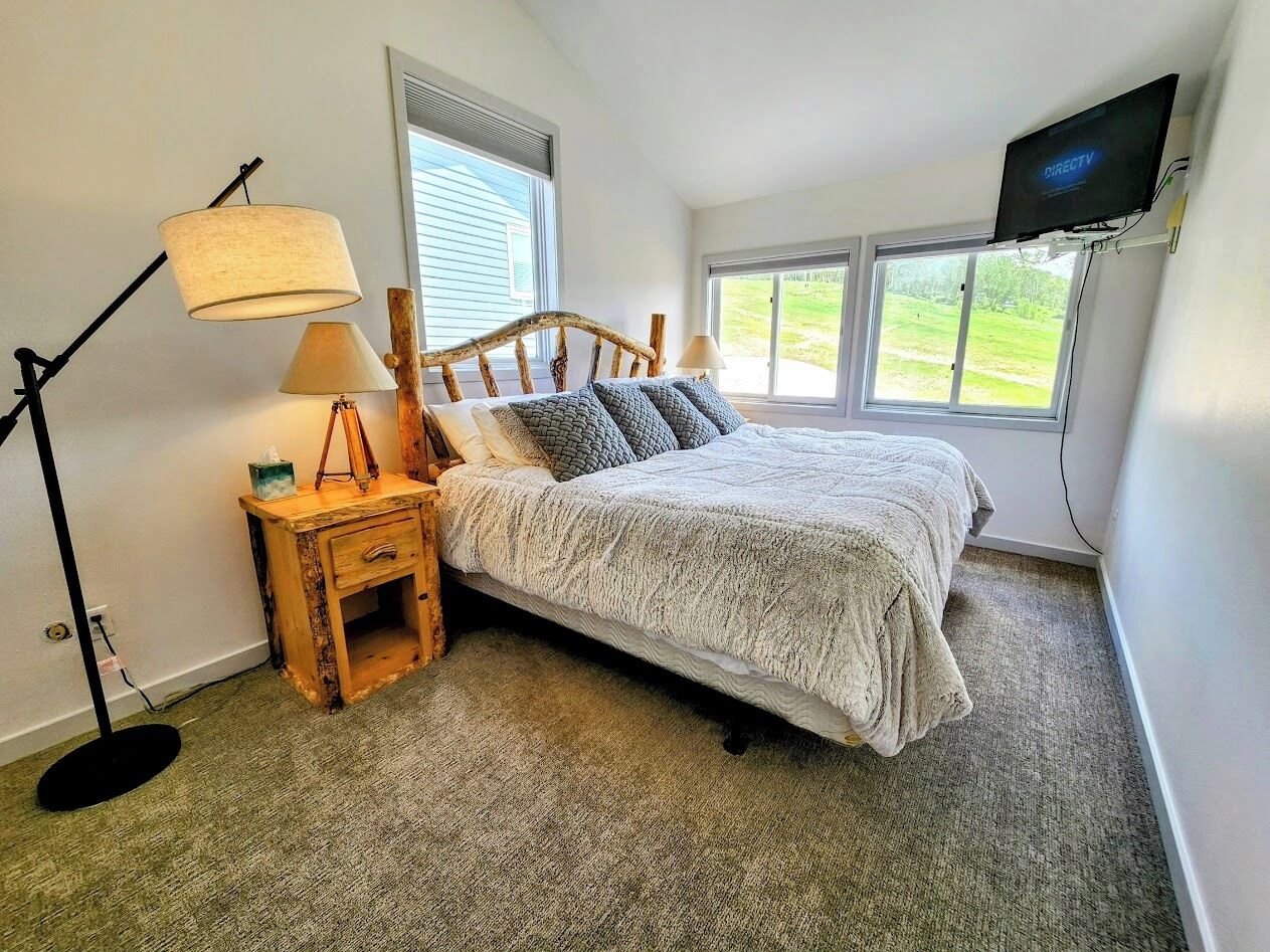 Une chambre à coucher comprenant un lit, une table de chevet, une lampe, un téléviseur et une fenêtre donnant sur l’extérieur.
