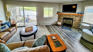A living room with a fireplace, a television, and a stone wall. - Ski-In Ski-Out Townhome | 2 Bedfroom | Shared Hot Tub | Fireplace | Parking (Mt. Crested Butte)