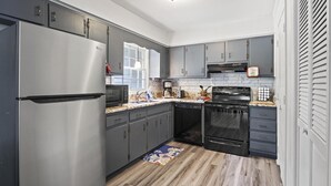 Een moderne keuken met grijze kastjes, roestvrijstalen apparatuur en een houten vloer.