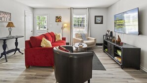 Een woonkamer met een rode bank, een witte fauteuil, een zwarte leren stoel, een klein rond tafeltje, een donker houten kast en een grote flatscreen-tv.
