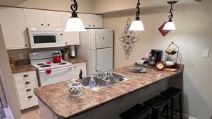 A kitchen with white cabinets, a granite countertop, a stainless steel sink, and a red kettle on the stove.