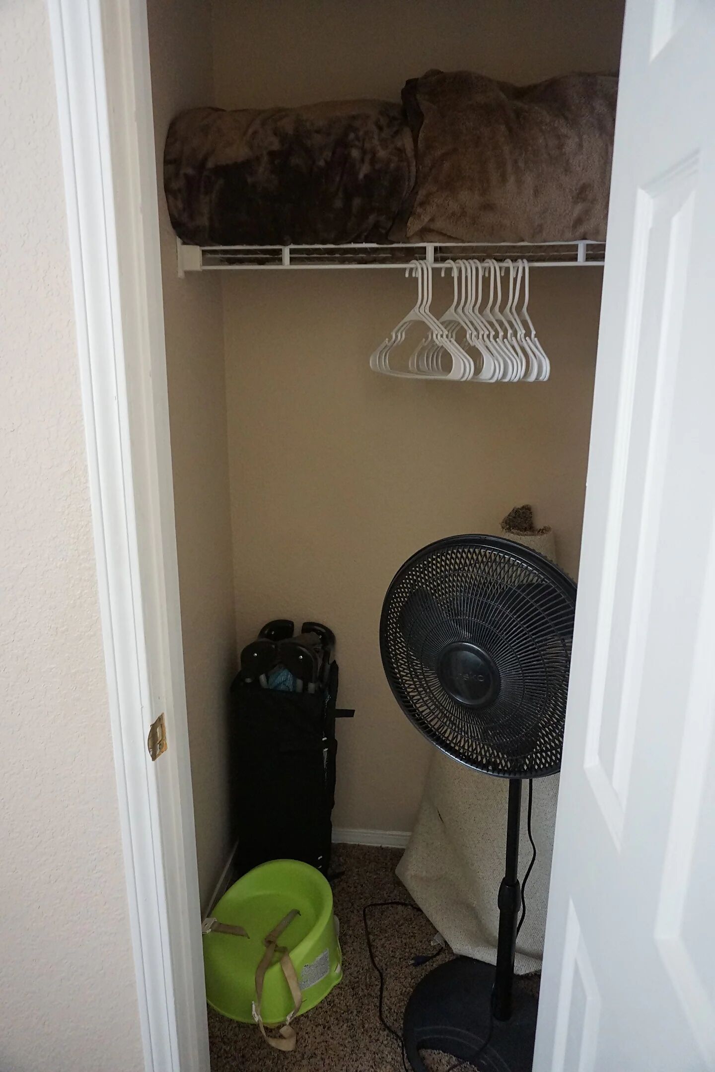 Een kleine kamer met een kast, daarin een bontjas, een ventilator en een groene emmer.