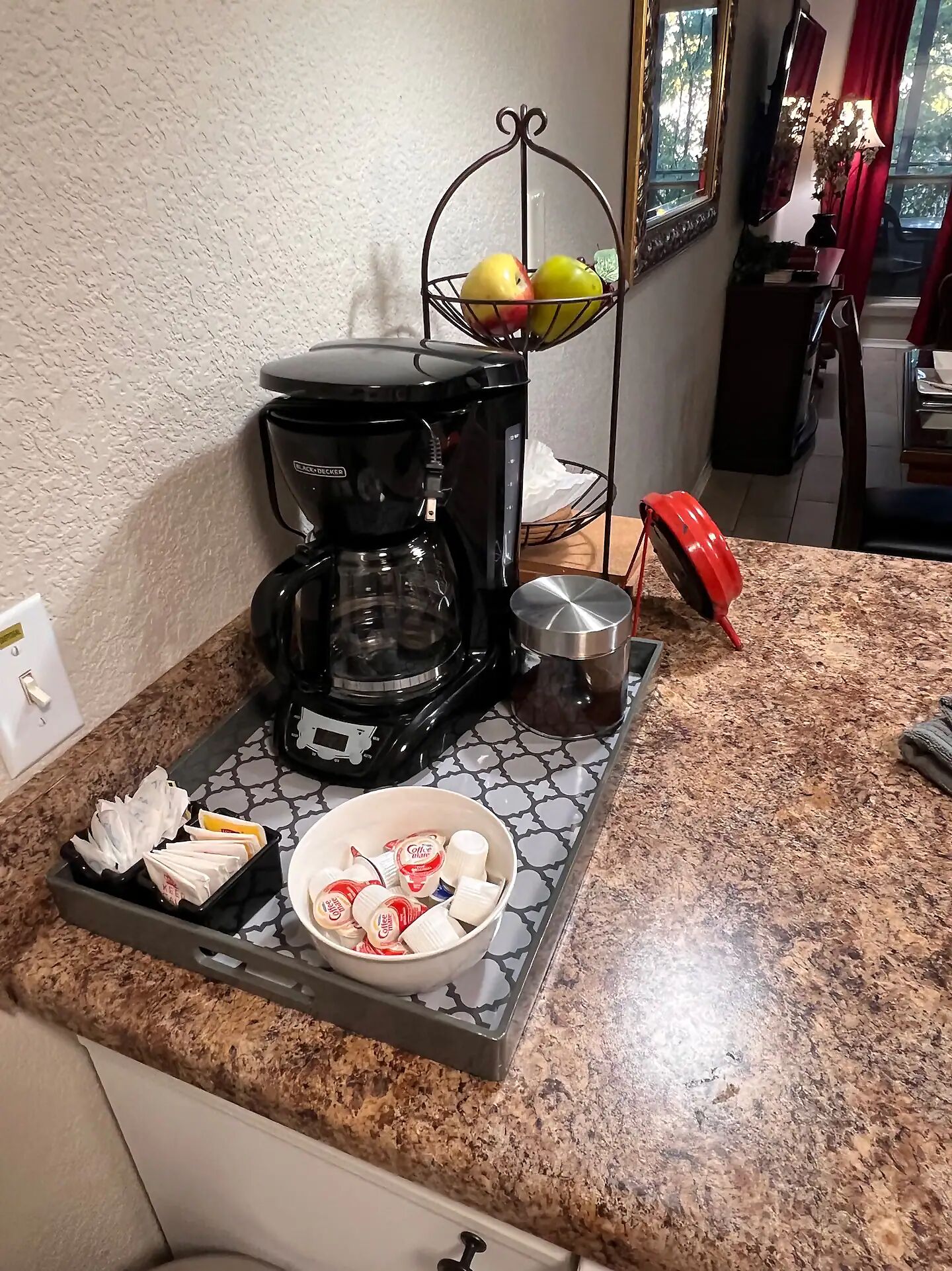 A kitchen counter with a coffee maker, a fruit basket, and a tray with coffee pods and napkins.