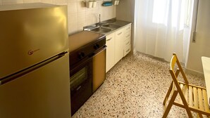 Una cocina compacta con refrigerador, estufa, lavamanos y alacenas.