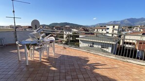 Una terraza en la azotea con suelo de baldosas, sillas de plástico blanco y una antena parabólica.