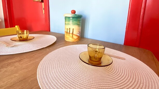 Una mesa de comedor con dos individuales y dos vasos, una puerta roja y una pared con un panel decorativo.