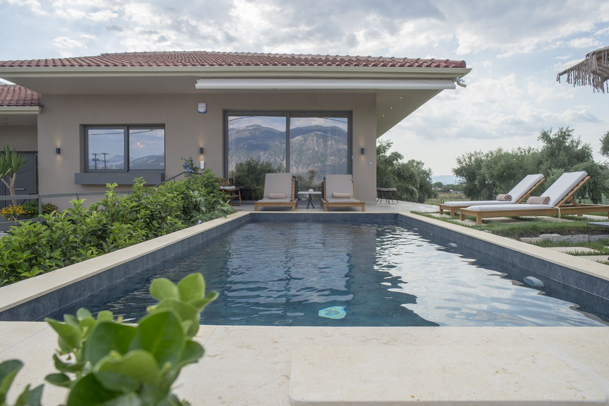 Una casa moderna con piscina, mobiliario exterior y vistas a la montaña.
