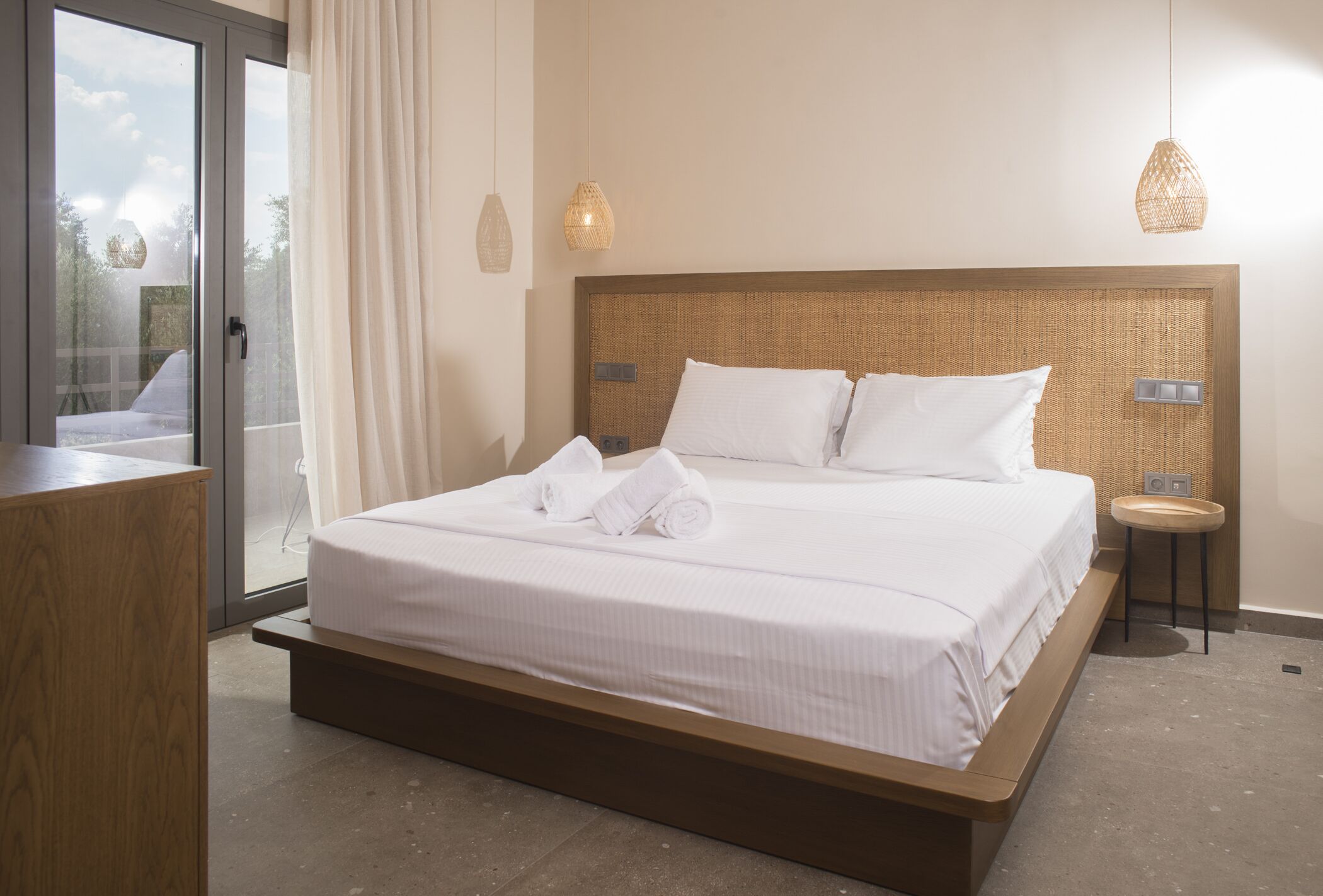 A neatly made bed with white linens and towels, a wooden headboard, and a small bedside table with a lamp.