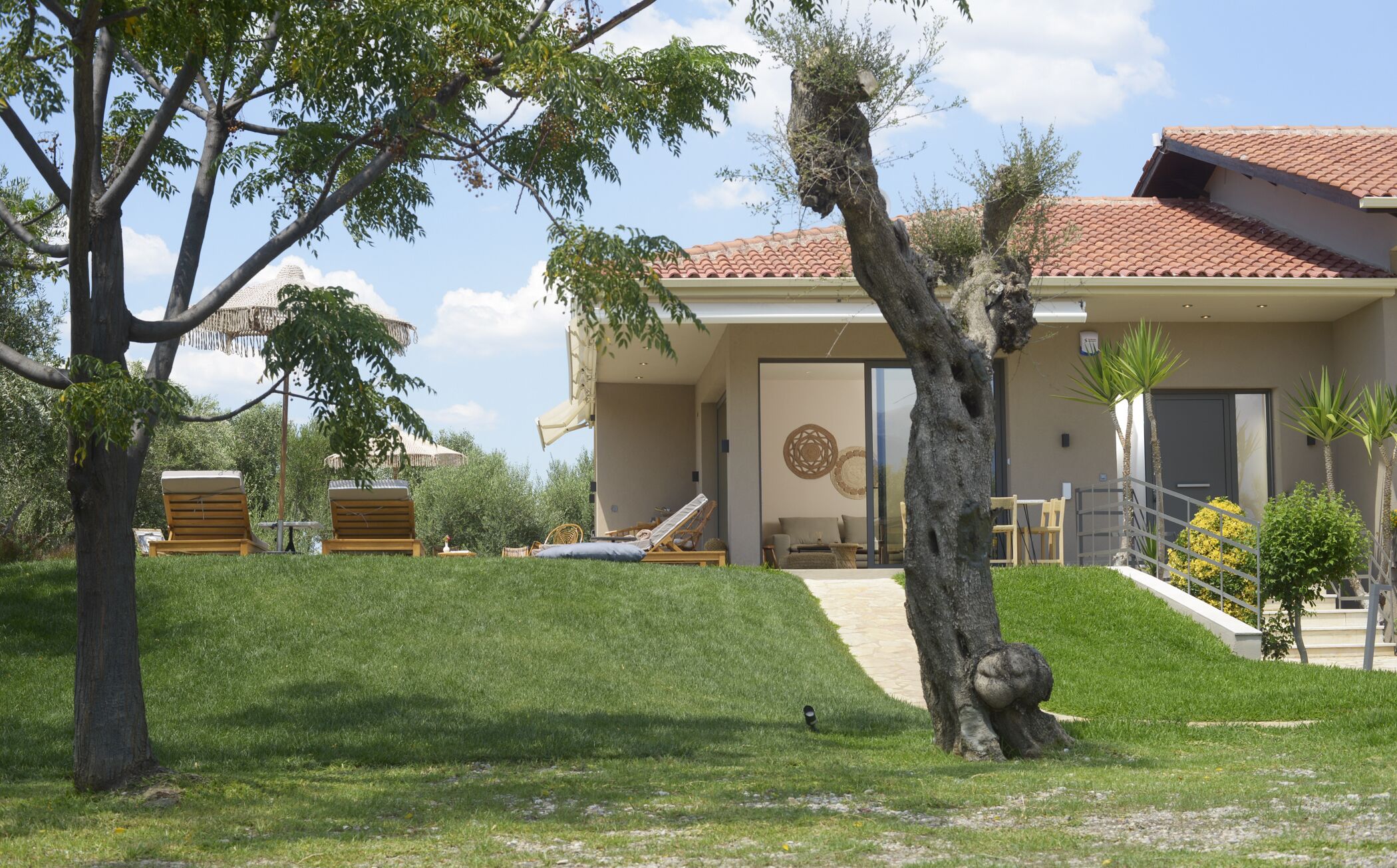 A modern house with a red-tiled roof, a covered patio, and a well-maintained lawn.