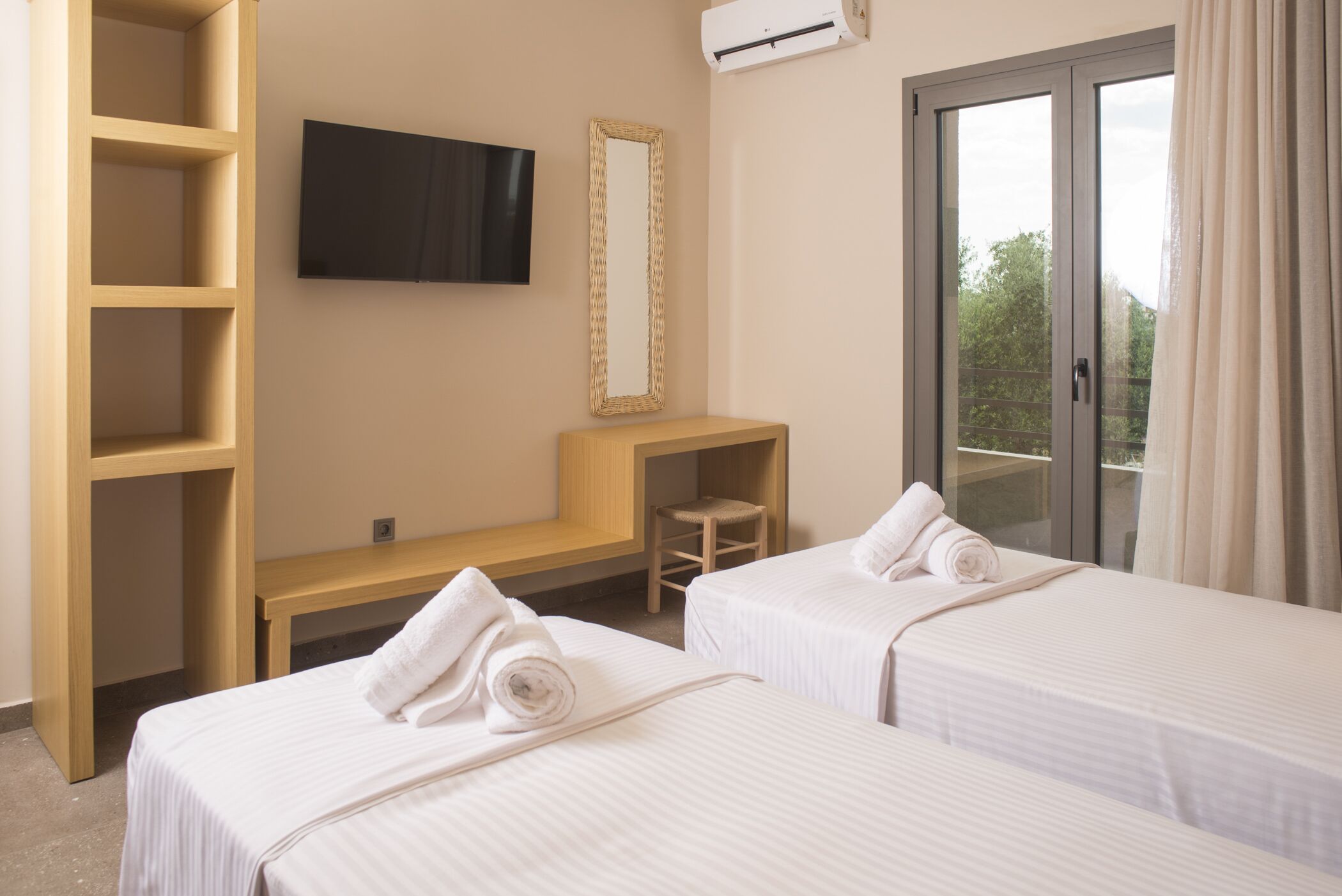 Habitación de hotel con dos camas, televisión, espejo y balcón con cortinas.