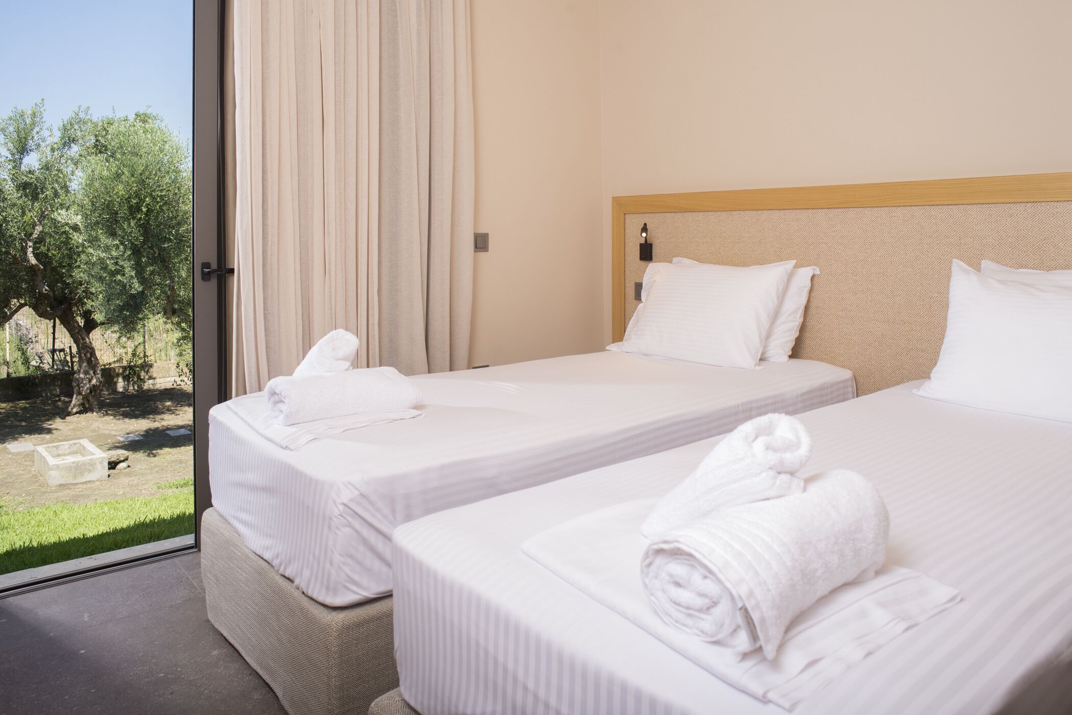 Habitació d'hotel amb dos llits, un finestral gran i vistes a la vegetació.