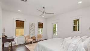 A bedroom with a large bed, two chairs, a desk, and a ceiling fan.