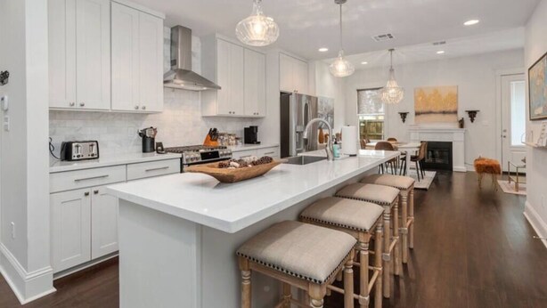 A modern kitchen with white cabinets, a large island with bar stools, and pendant lighting.