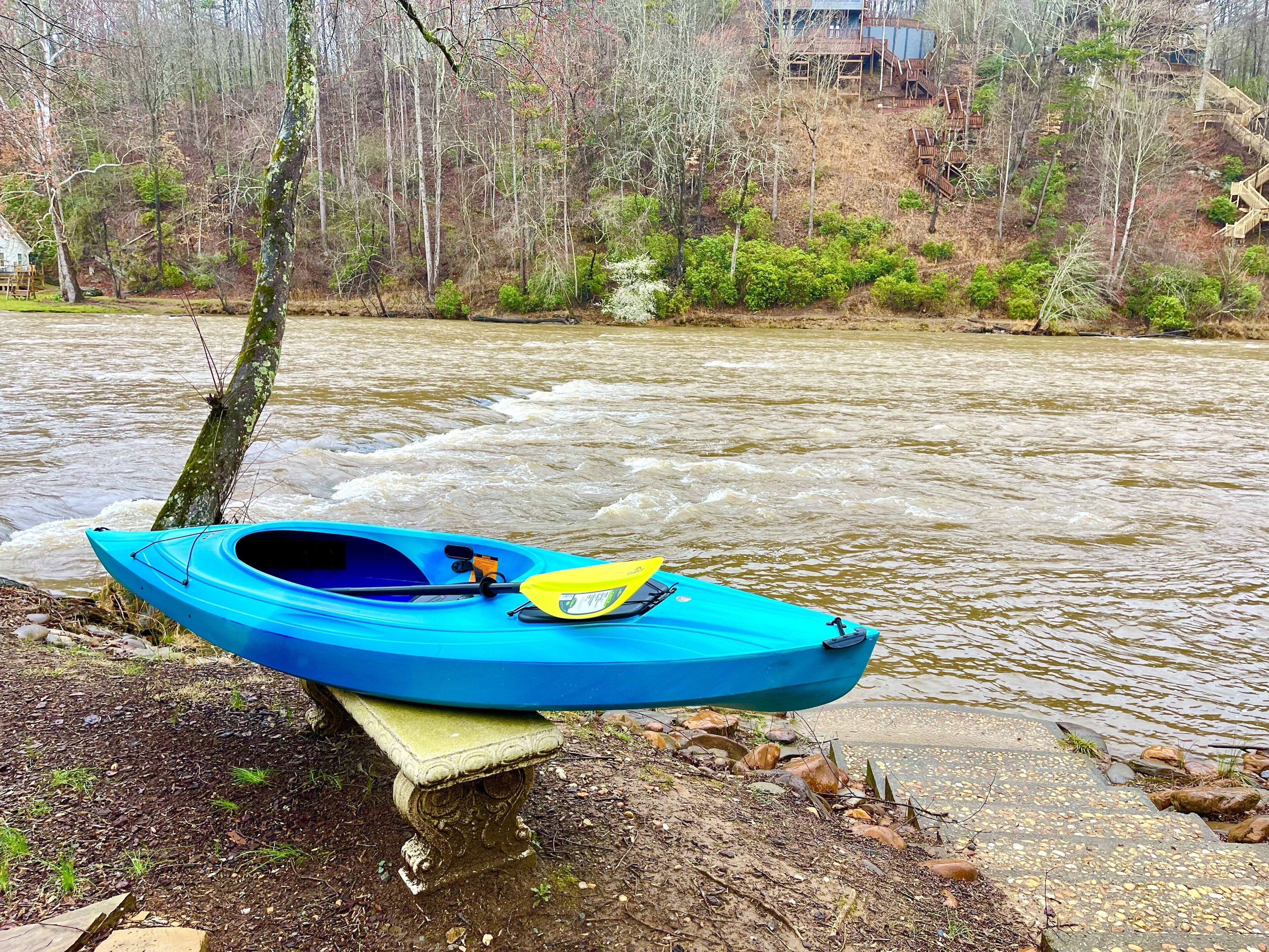 Un kayak bleu, avec une pagaie jaune posée sur une corniche rocheuse au bord d’une rivière.