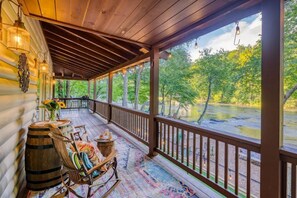 Une véranda couverte avec des balustrades en bois, des fauteuils à bascule et un tapis rustique.